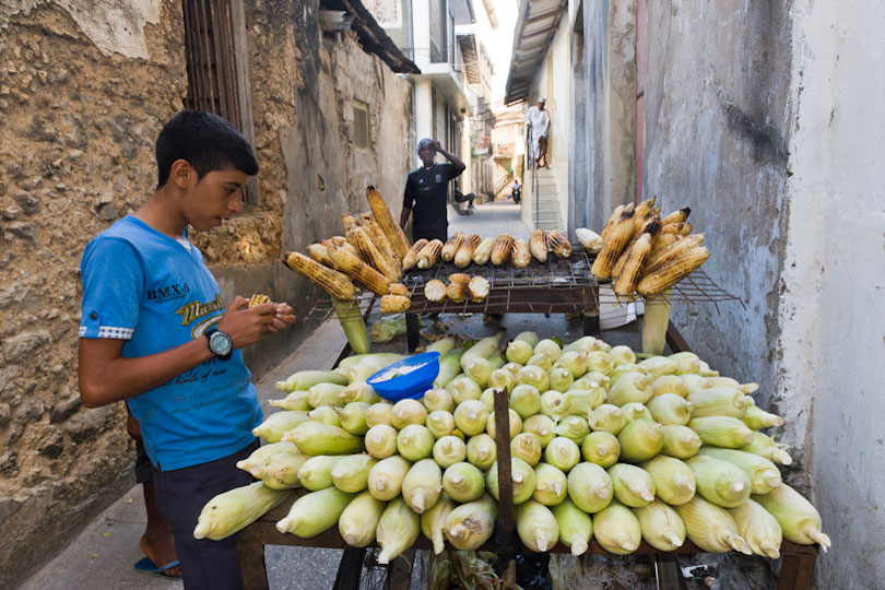 Boy buying grilled maize cobs from a food stand,&lt;p&gt; Stone Town, Zanzibar, Tanzania